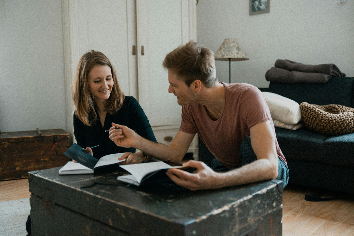 Paar sitzt am Couchtisch und schreibt gemeinsam Date-Ideen auf